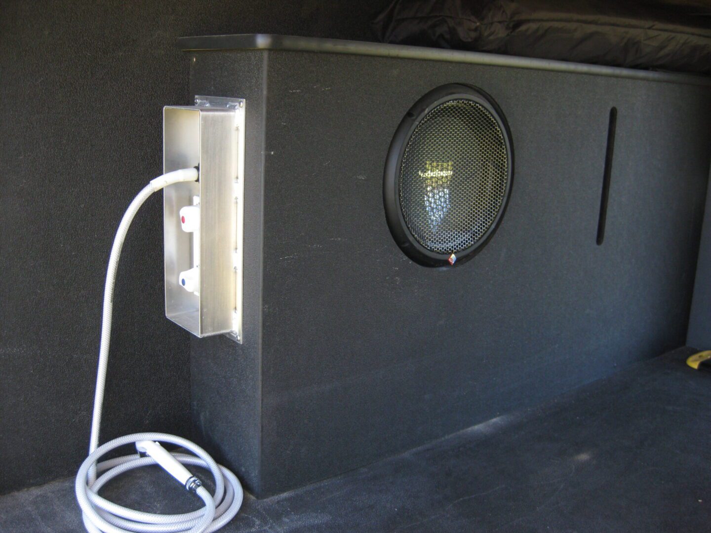 Interior view of a vehicle showing a black speaker integrated into the side panel and a white coiled hose connected to a fitting beside it.