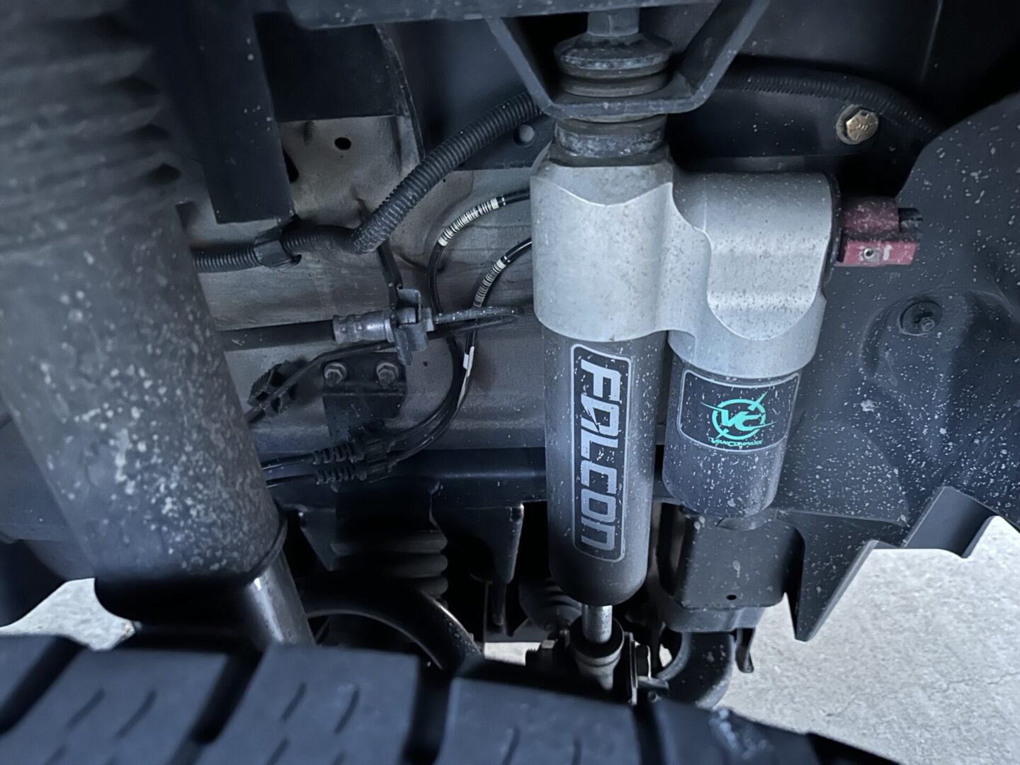 Close-up of a vehicle suspension system featuring a Falcon shock absorber. The surrounding components show minor dust and wear, with visible wiring and metal parts.